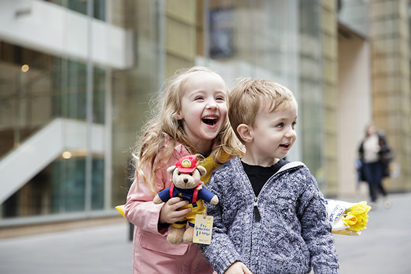 Two young children in Martin Place holding a Dougal bear and a bunch of daffodils Two young children in Martin Place holding a Dougal bear and a bunch of daffodils